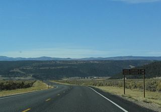 Signage for Losee Canyon and Casto Canyon, two areas located within Dixie National Forest that may be accessed by dirt and gravel roads, appears on westbound Utah 12. Both areas are located north of Utah 12. Utah 12, meanwhile, loses a bit of elevation as it reaches Bryce Canyon Junction and U.S. 89 in the distance.