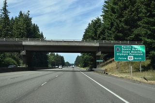 U.S. 101 (Olympic Loop Highway) begins from Interstate 5 at Exit 104, well beyond this sign preceding the SR 121 (93rd Avenue SW) overpass that references the Pacific Coast Scenic Byway encircling the Olympia Peninsula.