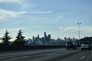Interstate 5 lines the hillside by Beacon Hill above the industrial plain to the west. The Downtown Seattle skyline remains in view northwest to the systems interchange (Exit 164 A) with Interstate 90.