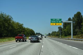 The entrance ramp from the weigh station forms an auxiliary lane to Exit 215. 300th Street NW heads west to Pioneer Highway (old SR 530) north of Stanwood.