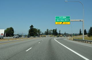 Interstate 5 reduces to four overall lanes at half diamond interchange (Exit 214) with Old Highway 99 S. Cederdale Road and Conway Frontage Road, service roads for I-5, tie into Old Highway 99 from the south nearby.