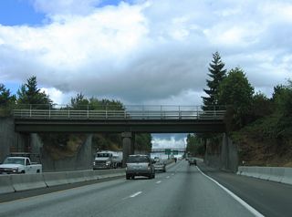 Interstate 5 ascends from the Alabama Street overpass through the Bellingham street grid to a commercial area anchored by Sunset Square shopping center along Sunset Drive east.
