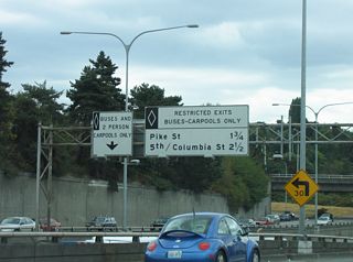 The next two exits of the Interstate 5 Express Lanes southbound are for Pike Street and 5th Street. Underway from August 2021 to May 2025, $68 million in road work at the exchange with SR 520 added a dedicated flyover for HOV-3 traffic between the Express Lanes and SR 520 (WSDOT, 2025).