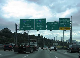 I-5 ascends onto a viaduct with five southbound lanes west of Capitol Hill. A lane drop occurs at Exit 167 for Mercer Street while the freeway mainline progresses toward Downtown Seattle and Interstate 90.