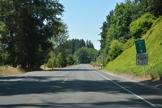 A sign for Business Loop I-5 stands along Huntington Avenue northbound between Larson Lane SW and Lions Pride Park along the Cowlitz River.