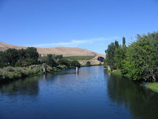 Remnant bridge supports remain in place just west of the SR 225 Yakima River span. A cut reveals the path of I-82/U.S. 12 beyond the river bend.