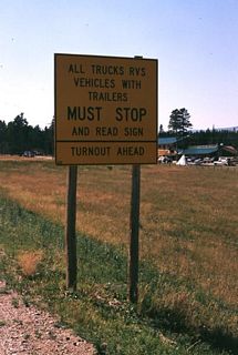 This sign (rectangular, in warning-sign colors) faces westbound traffic at Burgess Junction and advises truck and R.V. drivers that they must turn out and read a sign which contains a map of U.S. 14 and U.S. 14A between that crossroads and Cody, setting forth all the curves, downslopes, and engine and brake cooling points in color-coded symbology. The next picture shows the map. (It is difficult to determine the alphabet series used on this sign owing to the distorted perspective, but it is probably Series D.) Photo taken by Jonathan Winkler, 8/00.