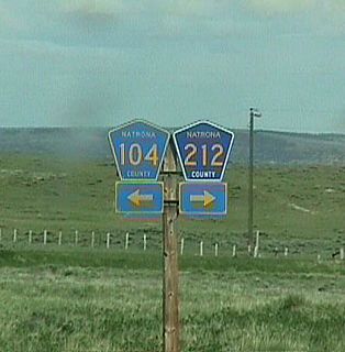 Eastbound U.S. 20-26 reaches its junction with Natrona County Route 104 and Natrona County Route 212. County Route 104 is Arminto Road (Waltman Road), and it leads to the site of Arminto next to the Burlington Northern Railroad tracks a couple miles north of U.S. 20-26. Natrona County Route 212 leads southwest along Gas Hills Road. Gas Hills Road turns west to cross into Fremont County, becomes Fremont County Route 267 (Dry Creek Road), then links with Wyoming 136 near the old uranium mines. Like many other states, Wyoming uses the standard blue and gold pentagon to mark its county routes.