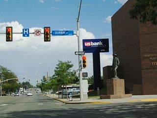 Continuing east, Business Loop I-25 south and U.S. 20-26 Business-87 encounter Durbin Street. A statue of a pioneer appears in Homestead Plaza next to a U.S. Bank branch.